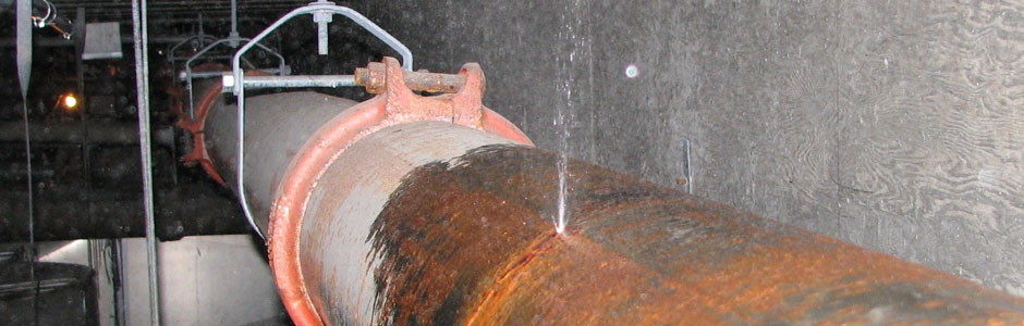 Water bursts through a pin hole on a stretch of corroded fire sprinkler pipe.